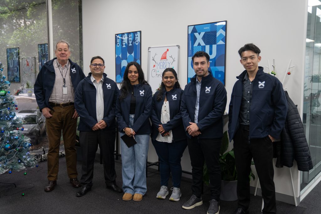 Xugar team members standing and wearing a bluish colored jacket showing "Xugar" logo on top right hand side